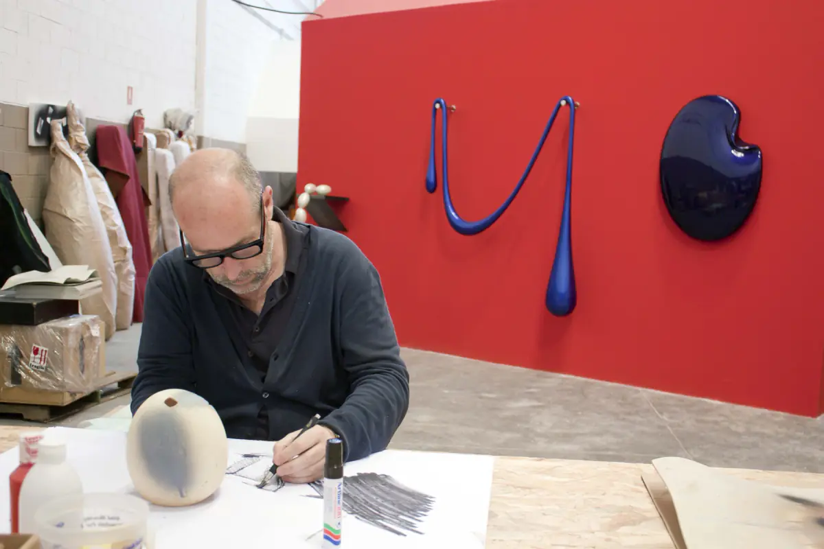 Santiago Villanueva dibujando en su taller, con sus esculturas al fondo